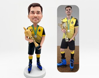 May include: A bobblehead figurine of a man in a yellow and black jersey, black shorts, and blue roller skates, holding a gold trophy. The figurine is on a white base. A second image shows a man in the same outfit holding a trophy.