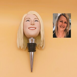 May include: A custom wine bottle stopper featuring a smiling face with blonde hair. The stopper has a silver metal base and a black rubber seal. The image also includes a small photo of a smiling woman with blonde hair.