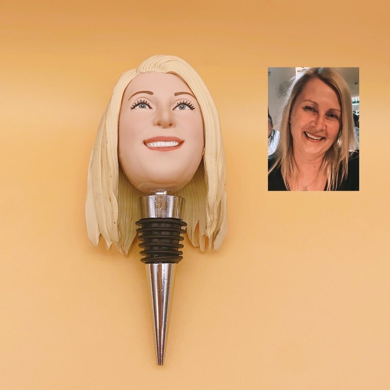 May include: A custom wine bottle stopper featuring a smiling face with blonde hair. The stopper has a silver metal base and a black rubber seal. The image also includes a small photo of a smiling woman with blonde hair.