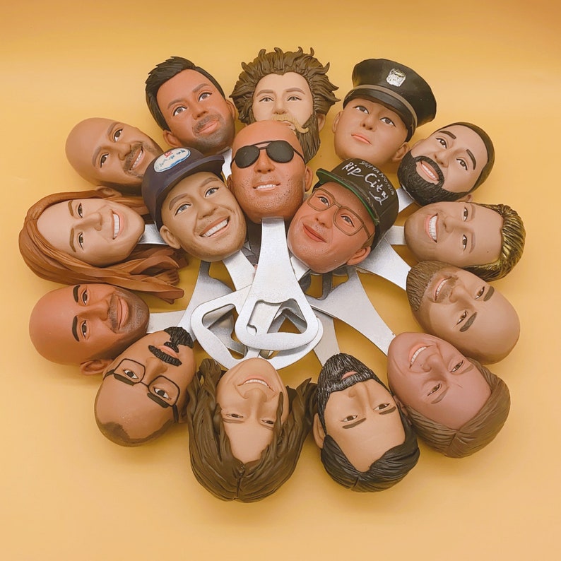 May include: A collection of novelty bottle openers, each featuring a detailed, sculpted head. The heads vary in skin tone, hair style, and facial expression. The openers are made of silver metal and are arranged in a circular pattern against a yellow background.