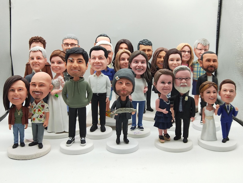 May include: A collection of custom bobblehead figurines featuring various individuals in diverse outfits, including wedding attire, casual clothing, and formal wear. Each figure stands on a circular white base, showcasing detailed facial features.