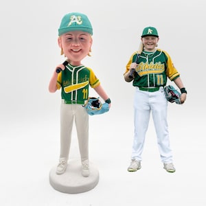 Puede incluir: Dos figuras de bobblehead con temática de béisbol y una persona con uniforme de béisbol. La figura de la izquierda es de una persona que lleva un uniforme de béisbol verde y amarillo con el número 11. La persona de la derecha lleva un uniforme de béisbol verde y amarillo con la palabra "Athletics" en la parte delantera.