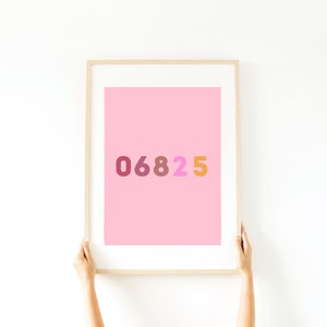 Op de afbeelding: Een ingelijst print met een roze achtergrond en de nummers 06825 in verschillende tinten rood, oranje en roze.