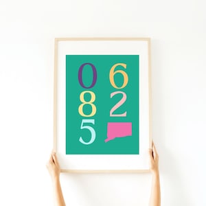 Op de afbeelding: Een ingelijst afdruk met een turquoise achtergrond en kleurrijke cijfers. De cijfers zijn 06825 en zijn gerangschikt in een verticale kolom. De staat Connecticut is in roze weergegeven aan de onderkant van de afdruk.