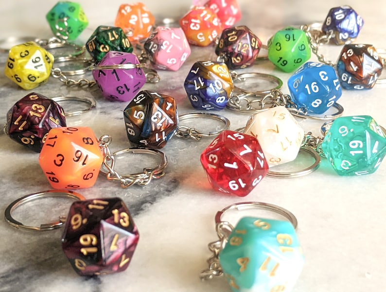 May include: A collection of colorful, multi-sided dice keychains. The dice are made of clear plastic with different colored swirls and have black numbers on them. The keychains are attached to silver metal rings.