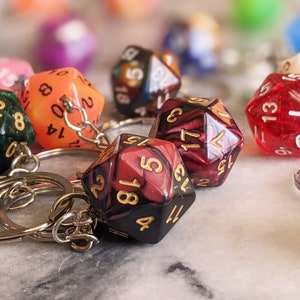 May include: A set of colorful, multi-sided dice with gold numbers attached to keychains. The dice are red, green, orange, black, and white.