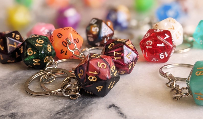 May include: A set of colorful, multi-sided dice with gold numbers attached to keychains. The dice are red, green, orange, black, and white.