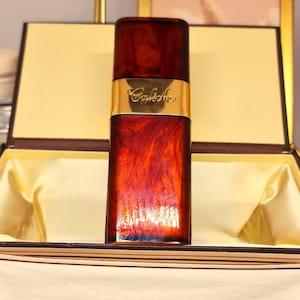 Puede incluir: Un frasco de perfume marrón y dorado con la palabra "Cacharel" en la etiqueta. El frasco está sentado en una caja blanca con un forro marrón.