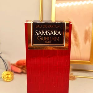 Może przedstawiać: Czerwone pudełko perfum Samsara Eau de Parfum firmy Guerlain, Paryż. Pudełko ma złote litery i czarną obw&oacute;dkę z napisem "EAU DE PARFUM" i "SAMSARA GUERLAIN PARIS". Pudełko zawiera 50 ml perfum.