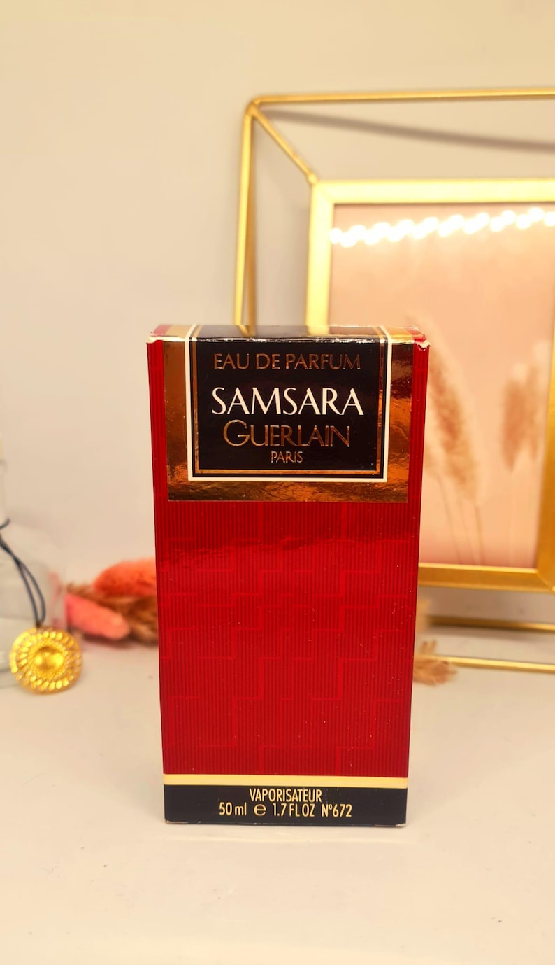 Może przedstawiać: Czerwone pudełko perfum Samsara Eau de Parfum firmy Guerlain, Paryż. Pudełko ma złote litery i czarną obw&oacute;dkę z napisem "EAU DE PARFUM" i "SAMSARA GUERLAIN PARIS". Pudełko zawiera 50 ml perfum.
