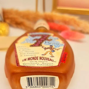 Pu&ograve; includere: Un flacone di profumo marrone con un'etichetta con la scritta "UN MONDE NOUVEAU..." e una grafica di una persona. L'etichetta include anche le parole "EAU DE TOILETTE" e gli ingredienti. Un codice a barre &egrave; visibile in basso.