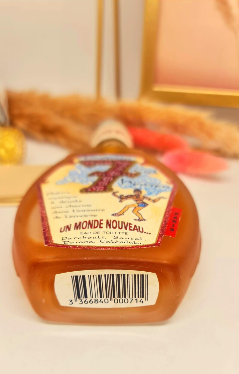 Pu&ograve; includere: Un flacone di profumo marrone con un'etichetta con la scritta "UN MONDE NOUVEAU..." e una grafica di una persona. L'etichetta include anche le parole "EAU DE TOILETTE" e gli ingredienti. Un codice a barre &egrave; visibile in basso.