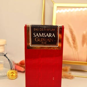 Może przedstawiać: Czerwone prostokątne pudełko perfum Samsara Guerlain. Pudełko ma złote litery i czarną podstawę. Tekst na pudełku brzmi "EAU DE PARFUM SAMSARA GUERLAIN PARIS NATURAL SPRAY 50 ml 1.7 fl oz N&deg;672".