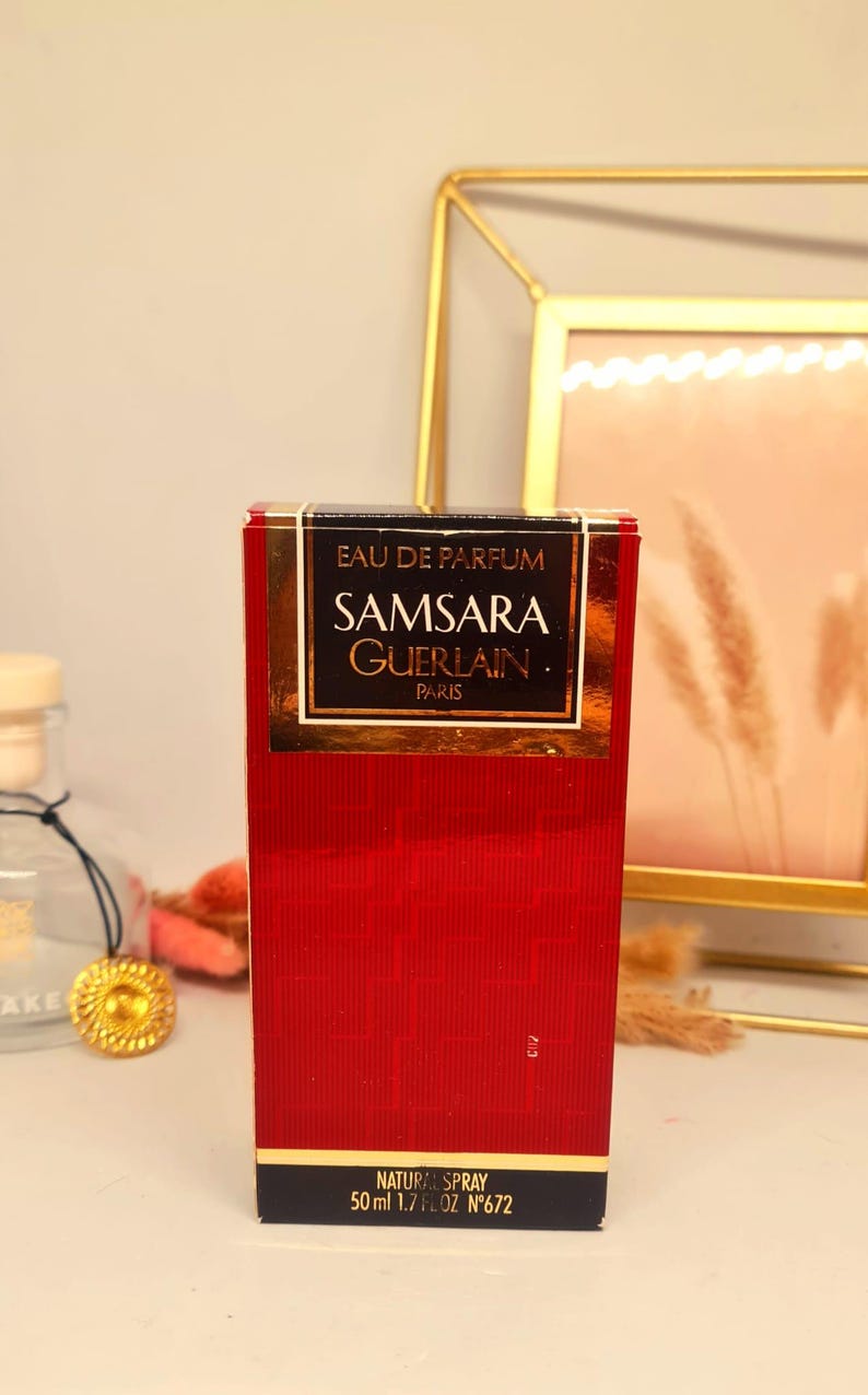 Może przedstawiać: Czerwone prostokątne pudełko perfum Samsara Guerlain. Pudełko ma złote litery i czarną podstawę. Tekst na pudełku brzmi "EAU DE PARFUM SAMSARA GUERLAIN PARIS NATURAL SPRAY 50 ml 1.7 fl oz N&deg;672".