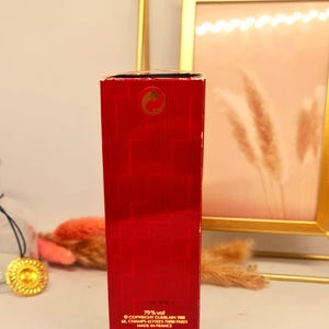 Może przedstawiać: Czerwone, prostokątne pudełko po perfumach ze złotymi akcentami. Na pudełku znajduje się tekst, w tym "79% vol" i "INGREDIENTS: ALCOOL PARFUM EAU". Pudełko znajduje się przed złotą ramką.