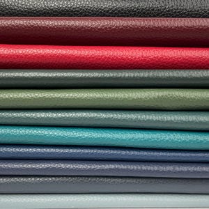 May include: A stack of various colored leather sheets. The colors include black, burgundy, red, dark gray, olive green, teal, navy blue, and light blue. The leather has a textured grain.