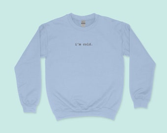 Puede incluir: Una sudadera de color azul claro con el texto "i'm cold." impreso en la parte delantera.
