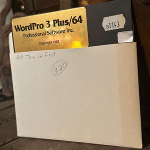 Puede incluir: Un disquete dorado y negro con la etiqueta "WordPro 3 Plus/64 Professional Software Inc. Copyright 1982" con el texto "Put This in first" y "320" escrito a mano en un sobre blanco.