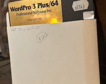 Könnte beinhalten: Eine goldene und schwarze Diskette mit der Aufschrift "WordPro 3 Plus/64 Professional Software Inc. Copyright 1982" und dem handschriftlichen Text "Put This in first" und "320" auf einem weißen Umschlag.