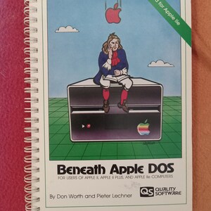 May include: A book cover with a cartoon illustration of a man sitting on a computer. The book title is "Beneath Apple DOS" and the subtitle is "For users of Apple II, Apple II Plus, and Apple Ile computers". The book is published by Quality Software.