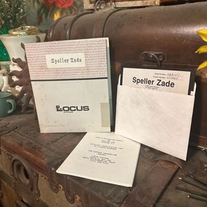 以下が含まれることがあります： 「Speller Zade」というラベルが貼られたビンテージフロッピーディスク。ラベルには「Locus Systems」というテキストが印刷されています。ディスクは、「ユーザーとインストールガイド Speller Zade」というテキストが印刷された白いスリーブに入っています。ディスクは木製のチェストの上に置かれています。