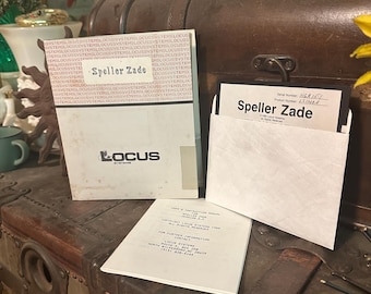 Könnte beinhalten: Eine Vintage-Diskette mit der Aufschrift "Speller Zade" und dem Text "Locus Systems" auf dem Etikett. Die Diskette befindet sich in einer weißen Hülle mit dem Text "Benutzer- und Installationshandbuch Speller Zade" auf der Vorderseite. Die Diskette liegt auf einer Holzkiste.