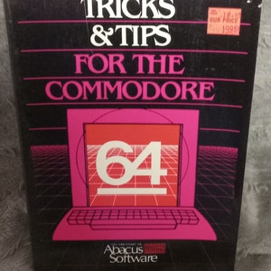 May include: A pink and black book titled "TRICKS & TIPS FOR THE COMMODORE 64" with a red and white logo of the Commodore 64 computer. The book is published by Abacus Software.