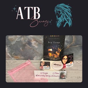 May include: A collection of items including a book titled "Ivy Love", stickers, a coaster, and a pink mesh bag. The book cover features a drink with ice. The text "ATB Swag" and a Native American headdress graphic are at the top.