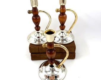 Puede incluir: Tres candelabros vintage. Cada uno tiene una base plateada, un centro de madera marrón oscuro y un asa dorada. Los candelabros están colocados encima de libros marrones. Los candelabros están diseñados para una sola vela.