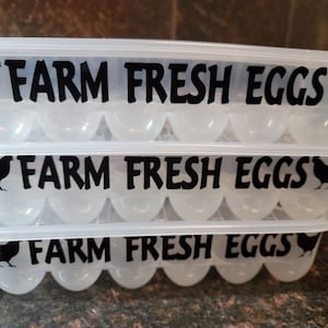 May include: Three clear plastic egg cartons stacked on top of each other. Each carton has a black silhouette of a chicken and the text "FARM FRESH EGGS" printed on the front.