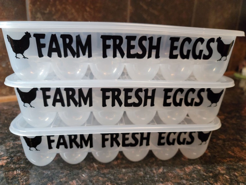 May include: Three clear plastic egg cartons stacked on top of each other. Each carton has a black silhouette of a chicken and the text "FARM FRESH EGGS" printed on the front.