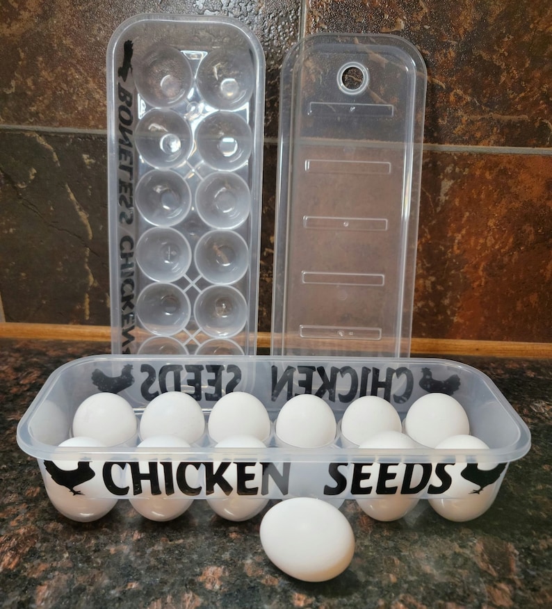 May include: A clear plastic egg carton with a black silhouette of a chicken and the text "Chicken Seeds" on the front. The carton is filled with white eggs.