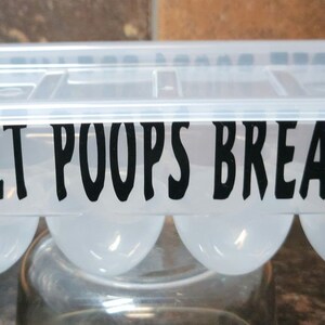 May include: A clear plastic egg carton with a black silhouette of a chicken on each end. The carton has a black label that reads "My Pet Poops Breakfast."