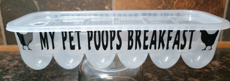 May include: A clear plastic egg carton with a black silhouette of a chicken on each end. The carton has a black label that reads "My Pet Poops Breakfast."
