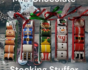 May include: Milk chocolate stocking stuffers in clear cellophane, each with a different Christmas design. Designs include a reindeer, nutcracker, elf, snowman, and Santa. Tied with red and green ribbons, and black and white checkered ribbon.