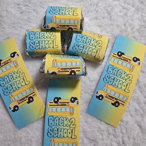 May include: Back to school themed candy wrappers and candy bars. The wrappers are yellow and blue with a school bus graphic and the text "BACK 2 SCHOOL". The candy bars are wrapped in foil.