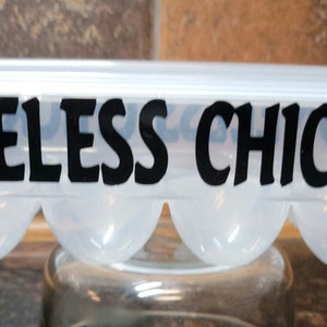 May include: A clear plastic egg carton with a black silhouette of a chicken on each end and the text "BONELESS CHICKEN" printed in black.