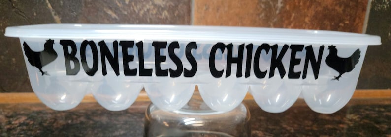 May include: A clear plastic egg carton with a black silhouette of a chicken on each end and the text "BONELESS CHICKEN" printed in black.