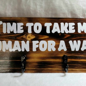 May include: A wooden sign with the text "TIME TO TAKE MY HUMAN FOR A WALK" in white letters. The sign has two black metal hooks on the bottom.