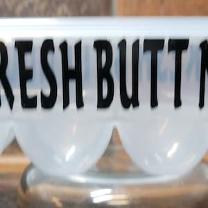 May include: White plastic egg carton with black chicken silhouettes and the text "FARM FRESH BUTT NUGGETS".