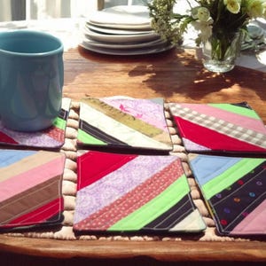 May include: Six colorful fabric coasters with a variety of patterns, including stripes, polka dots, and floral designs. The coasters are arranged on a wooden table with a blue mug in the background.