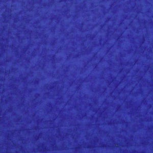 Op de afbeelding: Close-up van een gewatteerde stof in een diepblauwe tint. De stof heeft een getextureerde uitstraling met diagonale stiksels die een ruitpatroon cre&euml;ren. Een blauwgroene en blauwe patroonrand is zichtbaar aan de linkerkant.