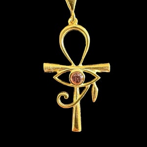 Op de afbeelding: Een gouden Ankh-ketting met een roze oog van Horus-bedel. De hanger is aan een gouden ketting.