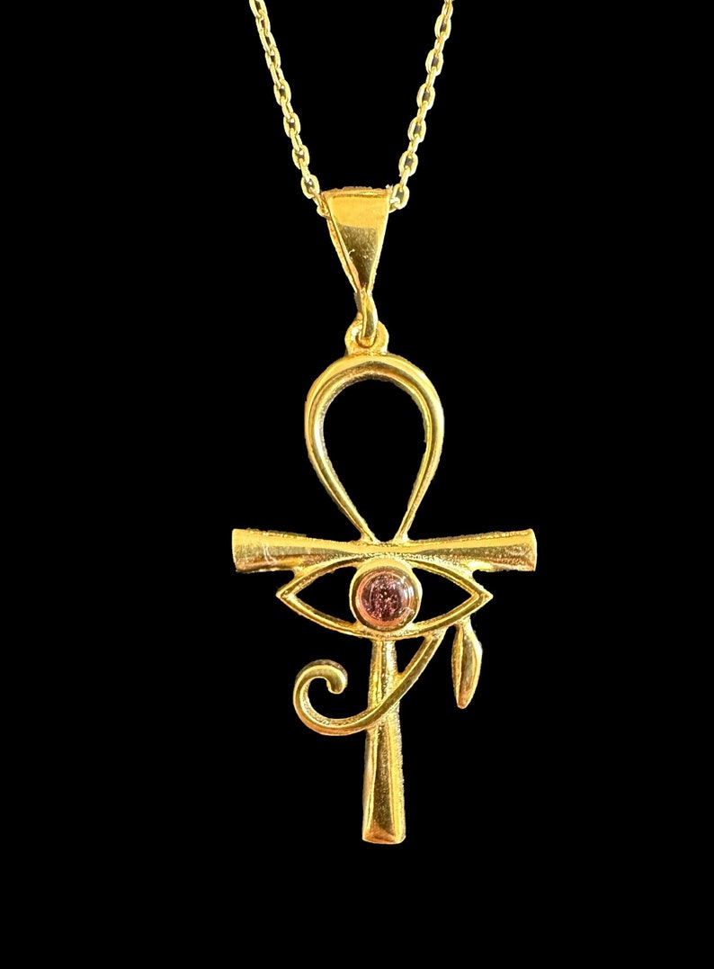 Op de afbeelding: Een gouden Ankh-ketting met een roze oog van Horus-bedel. De hanger is aan een gouden ketting.