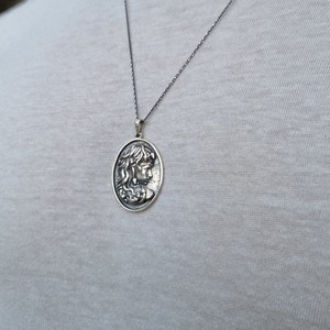 May include: A silver chain necklace with a pendant featuring a detailed profile of a woman's face.