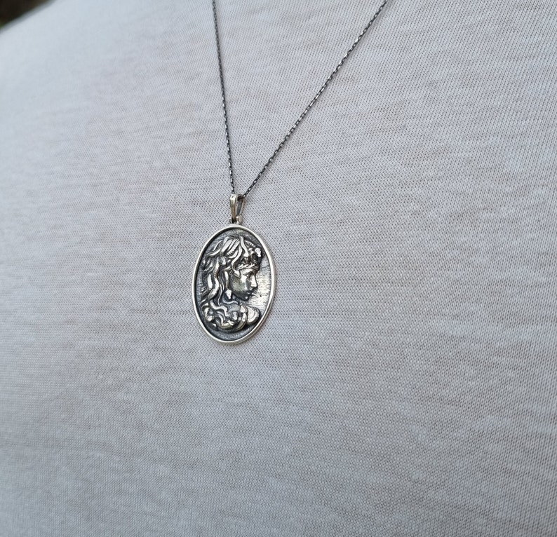 May include: A silver chain necklace with a pendant featuring a detailed profile of a woman's face.