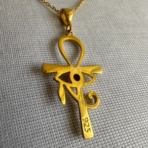 Op de afbeelding: Gouden ketting met hanger in de vorm van een Ankh-symbool met een rood oog van Horus in het midden. De hanger is aan de achterkant gemarkeerd met "925".