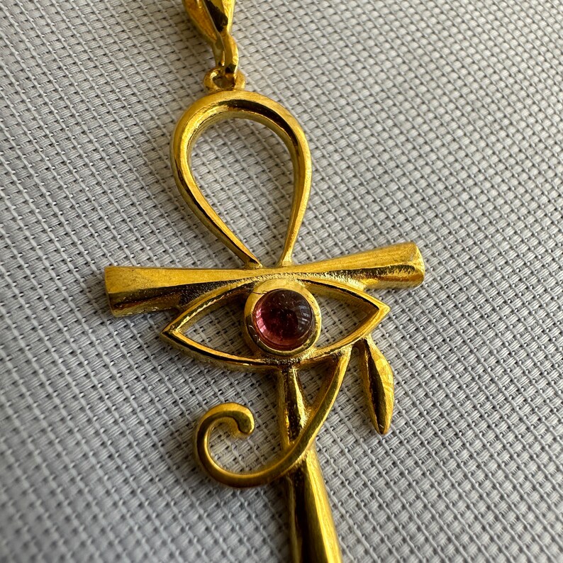 Op de afbeelding: Gouden hanger met een ankh met een roze oog van Horus.