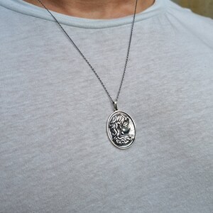 May include: A silver chain necklace with an oval pendant featuring a detailed profile of a woman's face.