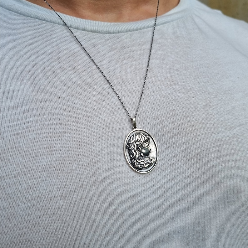 May include: A silver chain necklace with an oval pendant featuring a detailed profile of a woman's face.